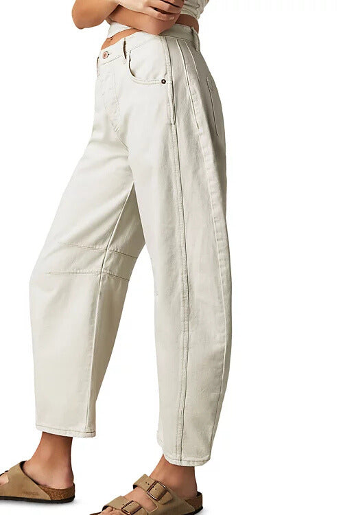 A person wearing Free People Good Luck Mid Rise Barrel jeans in off-white denim and tan sandals stands against a white background, shown from waist to feet in a side view.