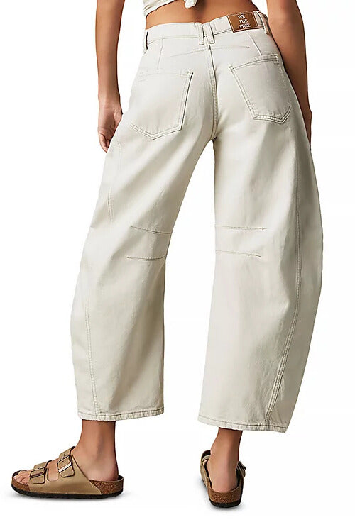 Model wears the Good Luck Mid Rise Barrel jeans by Free People in light beige, featuring back pockets, paired with tan sandals. Shown from behind against a plain white background.