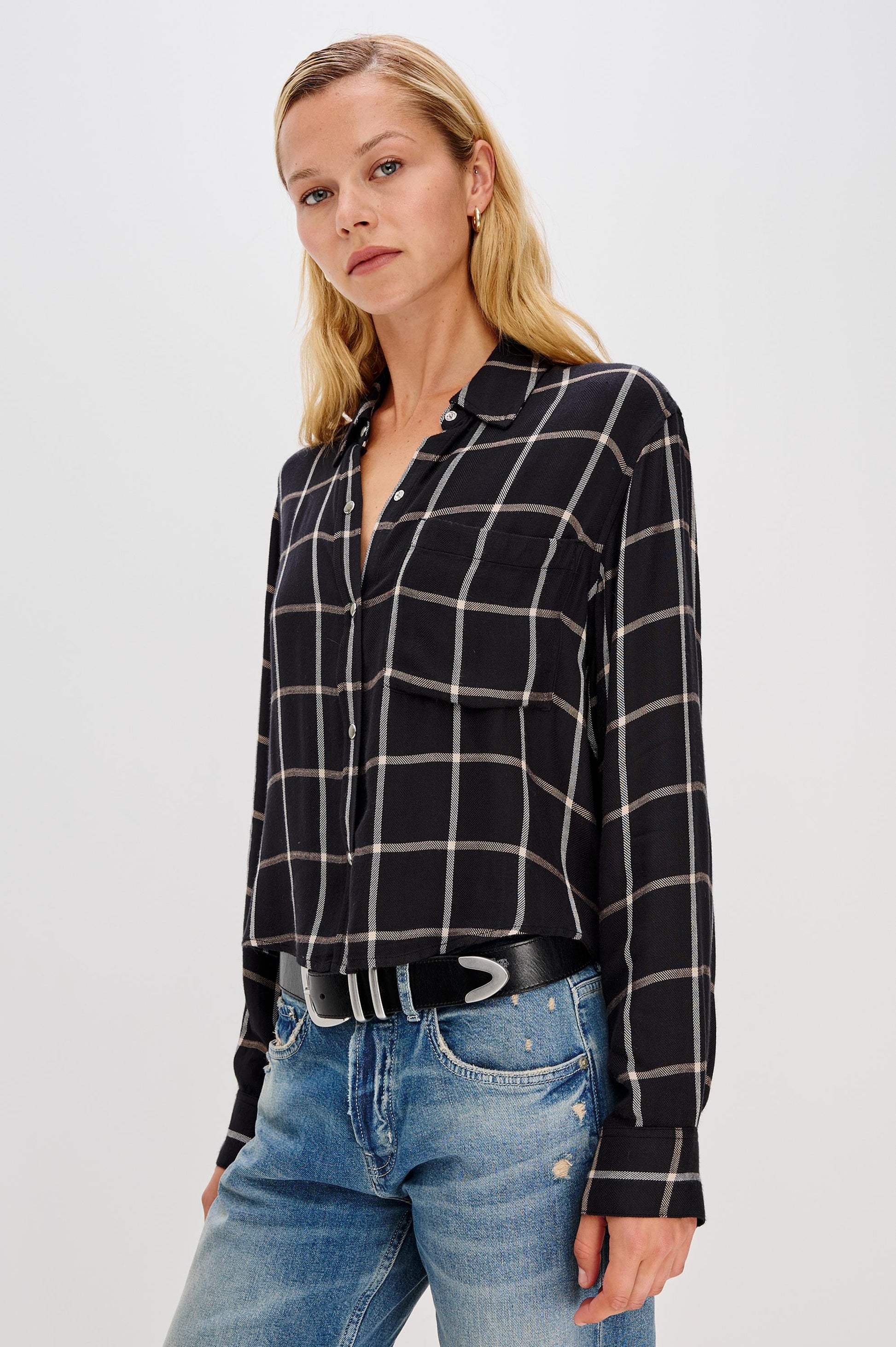 A woman with long blonde hair wears the Rails Malin Long Sleeve Check shirt in black and white, paired with light blue distressed jeans and a black belt, standing against a plain white background.