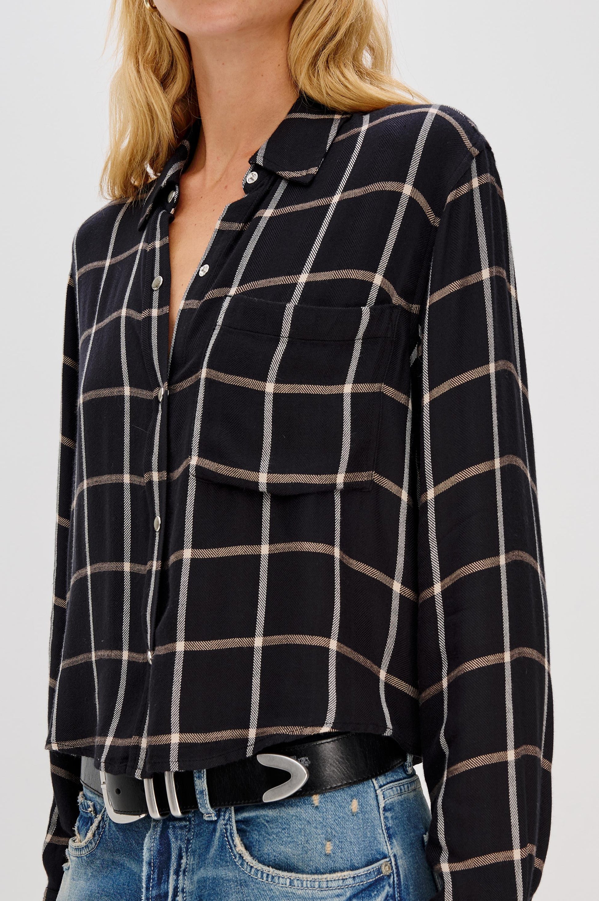 A person wears the Rails Malin Long Sleeve Check shirt in a relaxed fit black and beige plaid with front pockets, blue jeans, and a black belt. The 100% rayon shirt is hand wash cold recommended. Image cropped at shoulders and hips.