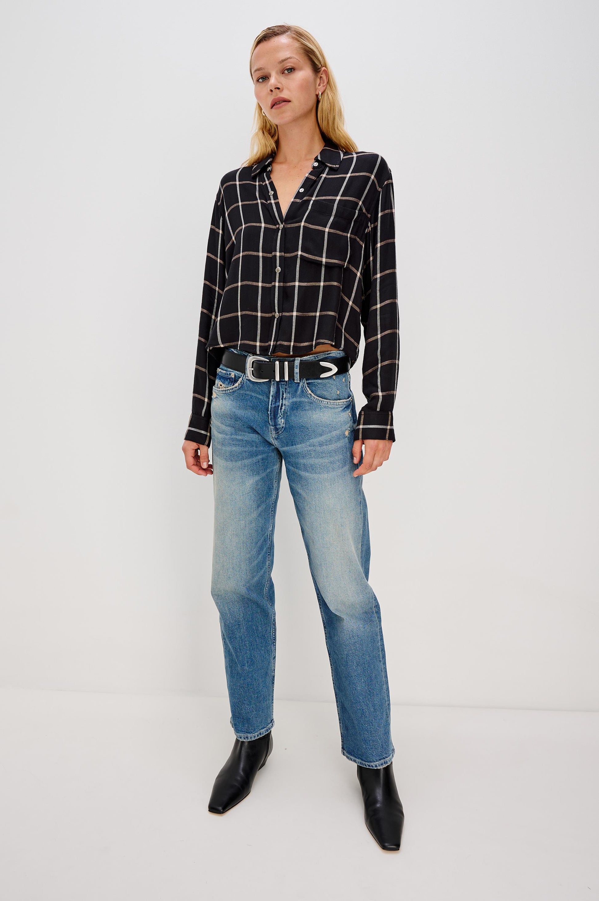 A woman stands against a white background wearing the Rails Malin Long Sleeve Check shirt in black with a white windowpane pattern, 100% rayon, paired with light blue straight-leg jeans, a black belt with silver details, and black ankle boots. Hand wash cold.