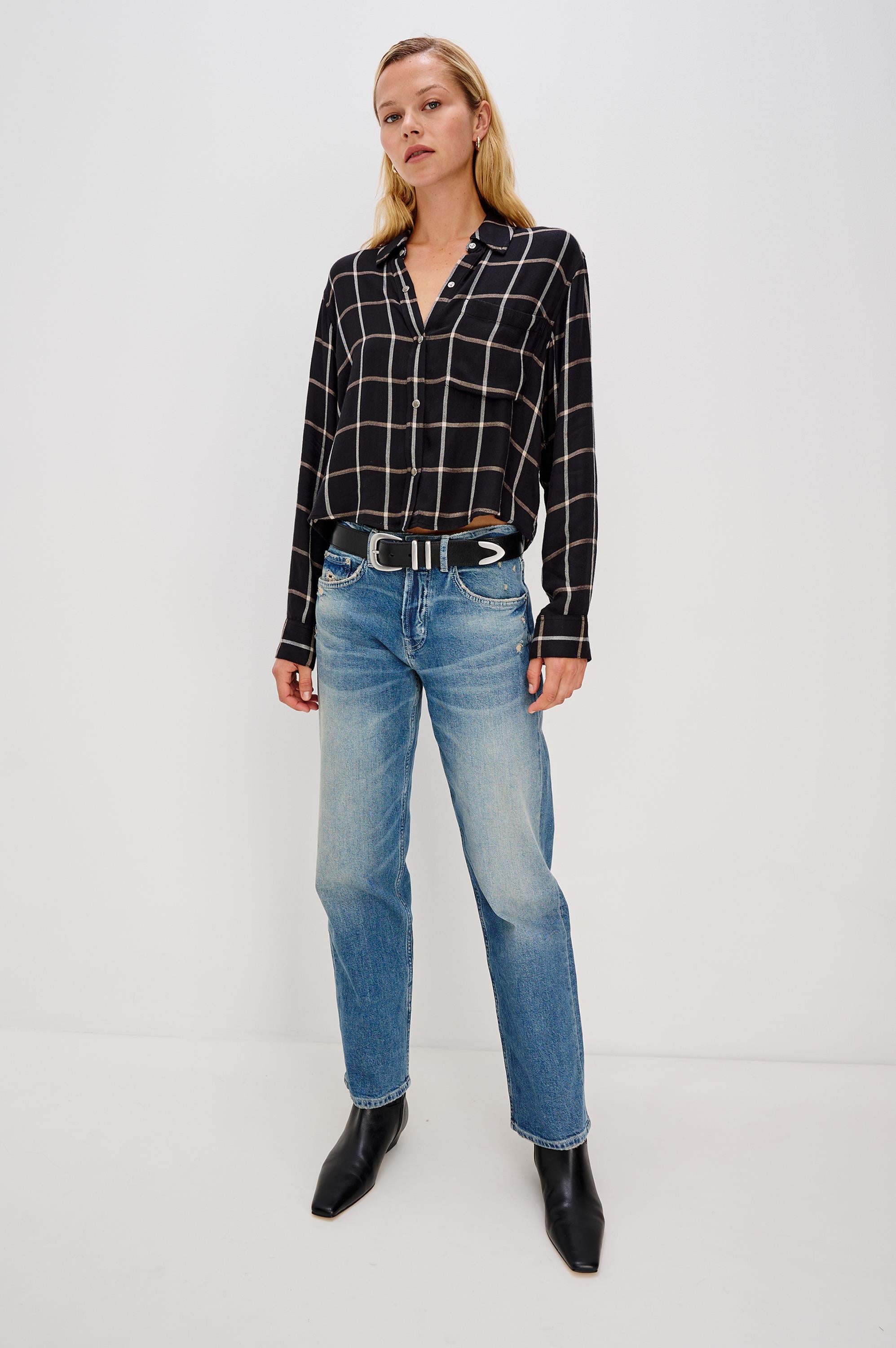 A woman stands against a white background wearing the Rails Malin Long Sleeve Check shirt in black with a white windowpane pattern, 100% rayon, paired with light blue straight-leg jeans, a black belt with silver details, and black ankle boots. Hand wash cold.