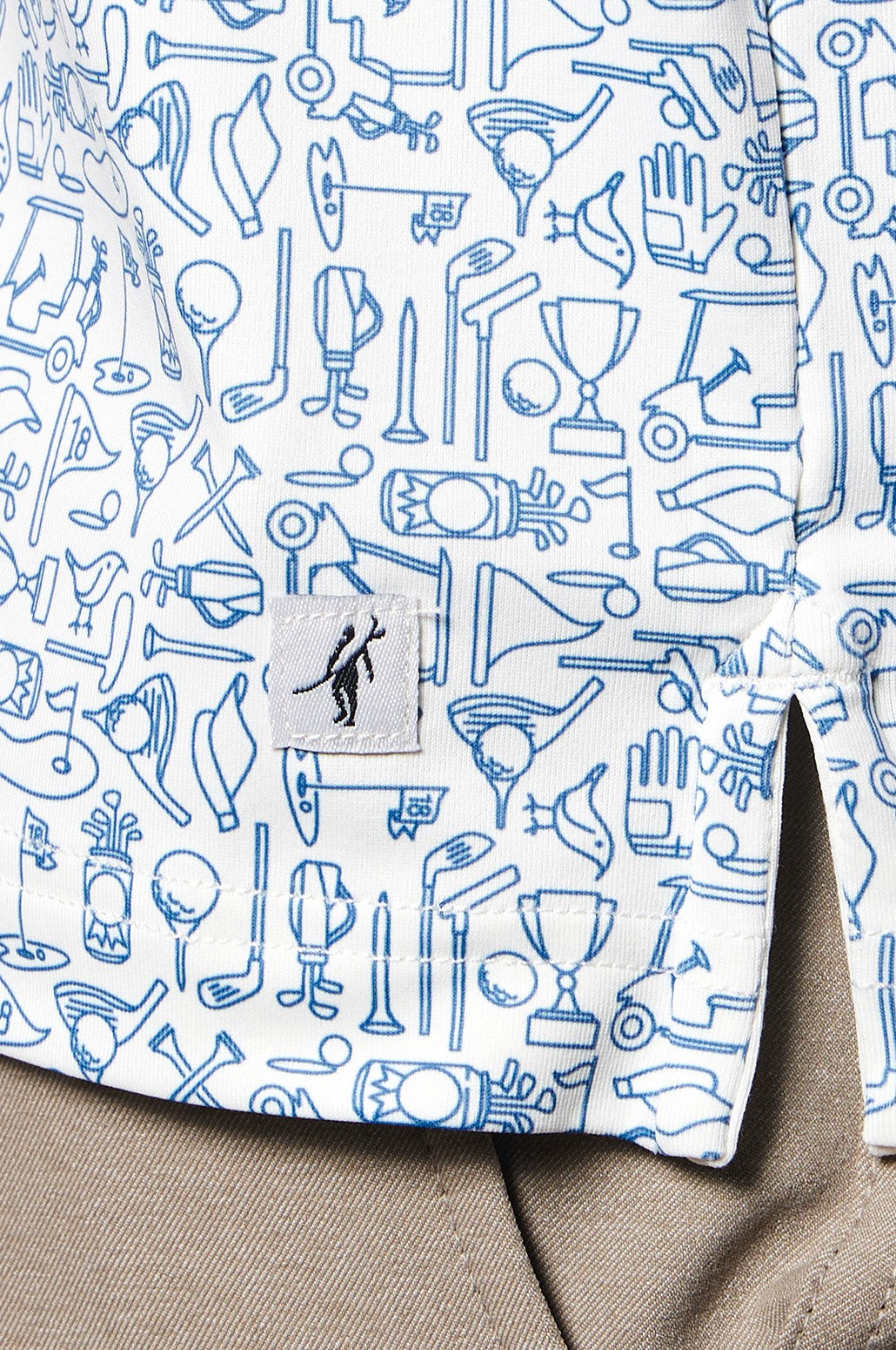 Close-up of the Clubhouse Polo Tequila Therapy by Toes on the Nose, a white moisture-wicking shirt with blue sports-themed doodles and a golfer logo tag near the hem, paired with beige pants.