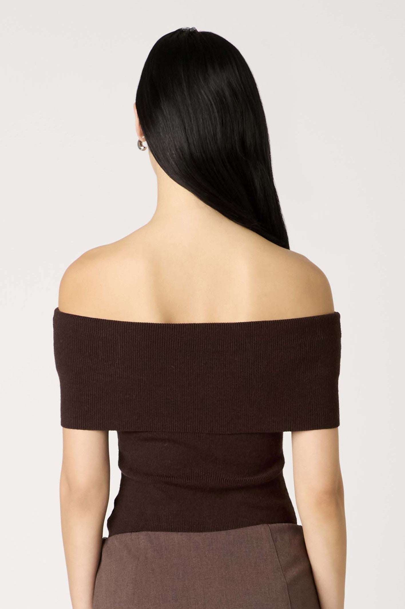 A woman with long, straight black hair is shown from the back wearing the Nia Annemarie Sweater in dark brown and brown pants against a plain light background.