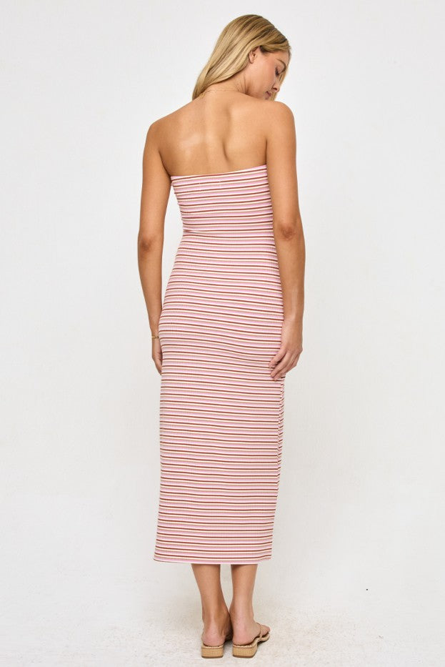 A woman stands facing away, wearing the L*Space Lisette Midi Dress—a strapless, form-fitting silhouette with bold red and white stripes—paired with flat sandals. Crafted from viscose elastane, the dress accentuates her figure as she showcases her blonde hair against a plain white background.