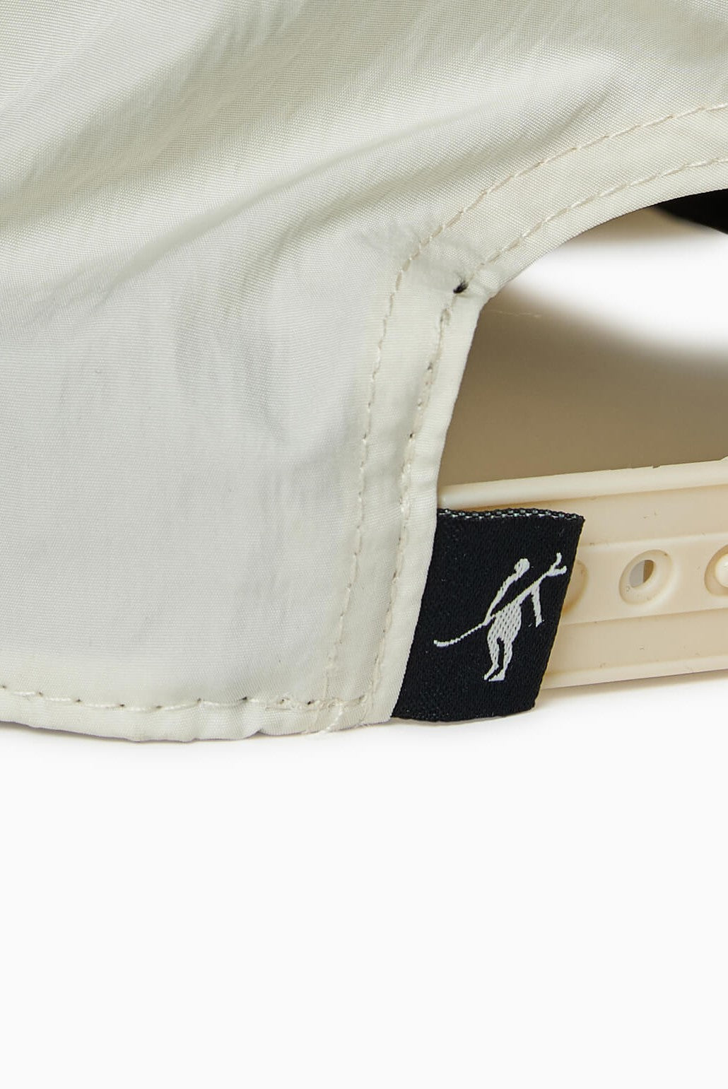 Close-up of the back of a Toes on the Nose Captain Cocktail Hat, a beige 5 panel unstructured cap with an adjustable snapback and a small black tag showing a white silhouette of a person holding a stick or bat.