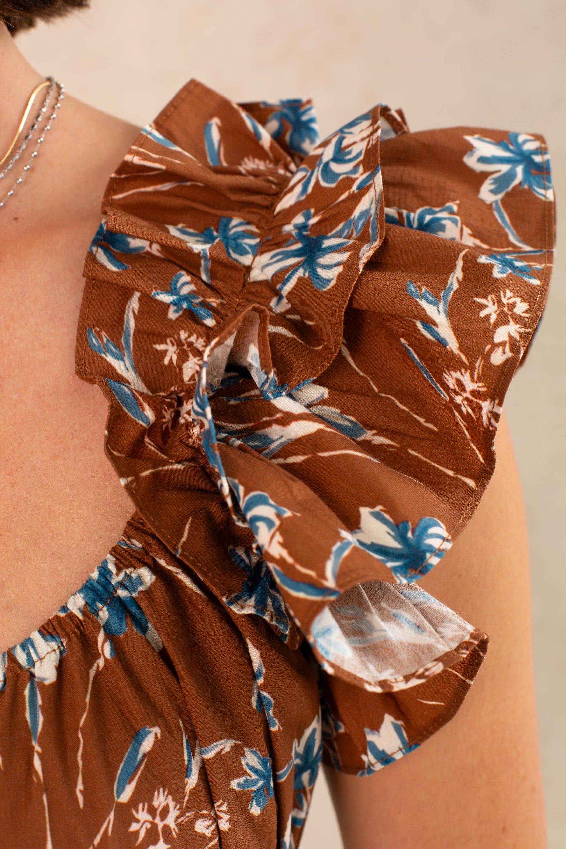 Close-up of the Georgie Avery Top in Brown Floral, featuring blue and white floral print, ruffle sleeves, and a delicate smocked bodice detail. A portion of a silver necklace is visible on the person's neck.