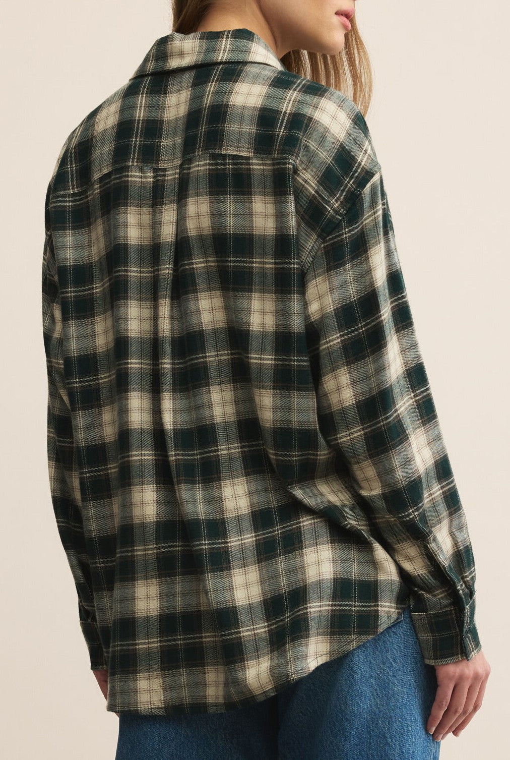 A person wearing the Z Supply River Plaid Button Up in Garland Green with blue jeans, shown from the back and slightly turned to the side.