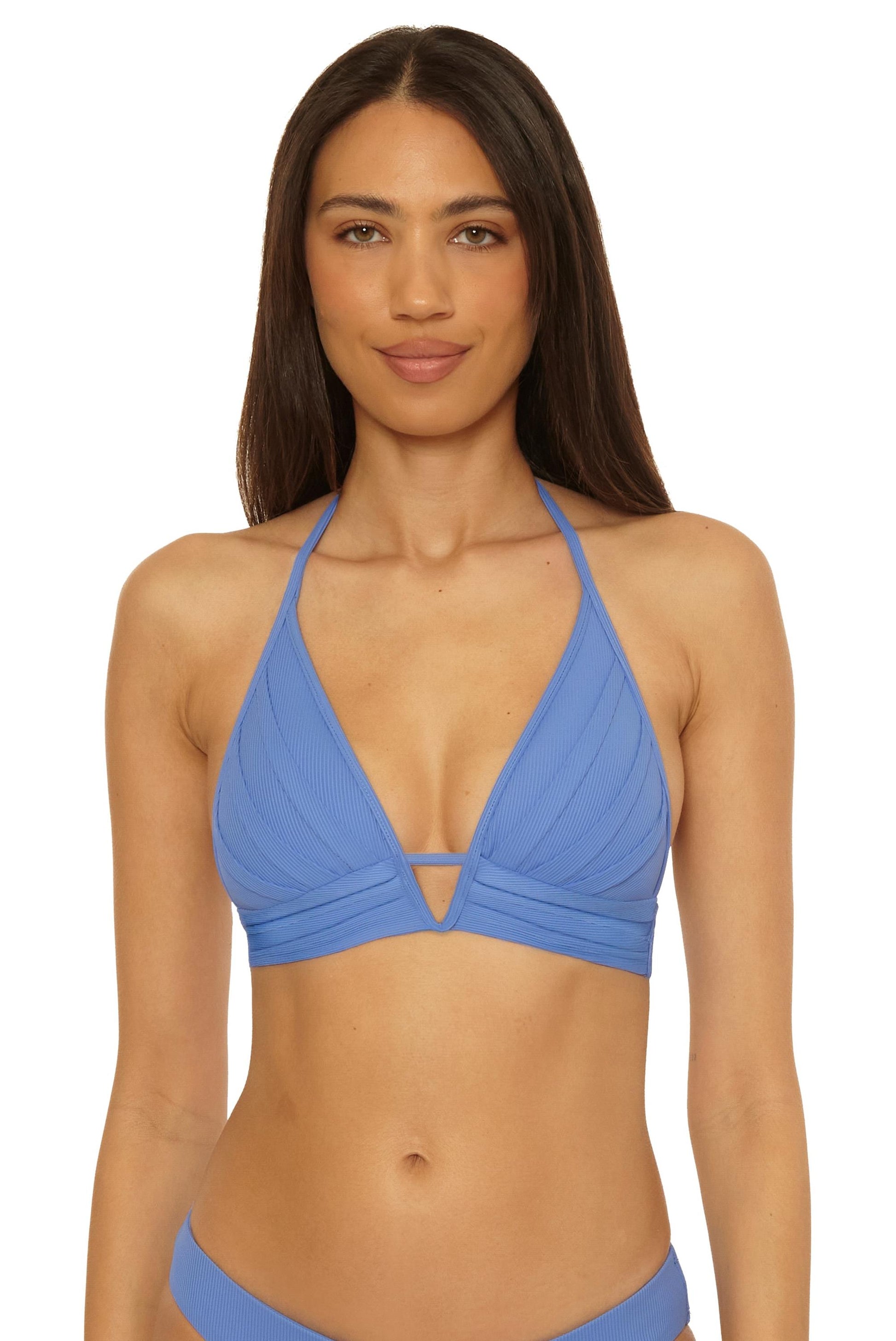 A woman models the Becca Swim Modern Edge Halter in COASTAL, a ribbed light blue bikini top with adjustable tie, removable soft cups, and V-neckline, standing against a plain white background.