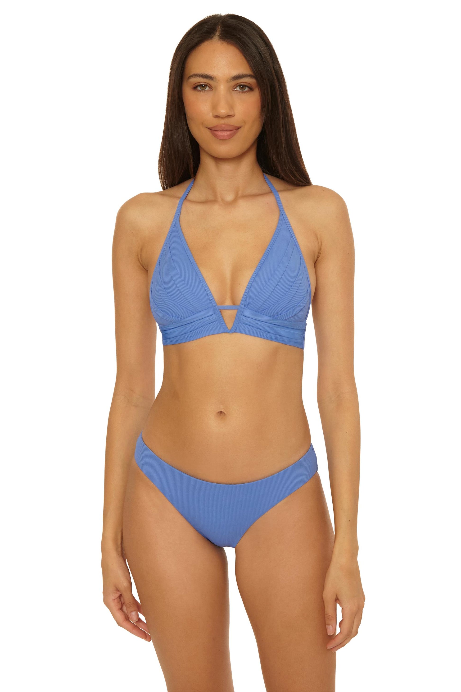 A woman with long straight brown hair poses against a plain white background, wearing the Becca Swim Modern Edge Halter in Coastal—a light blue bikini top with removable soft cups and matching bottoms—with a neutral expression.