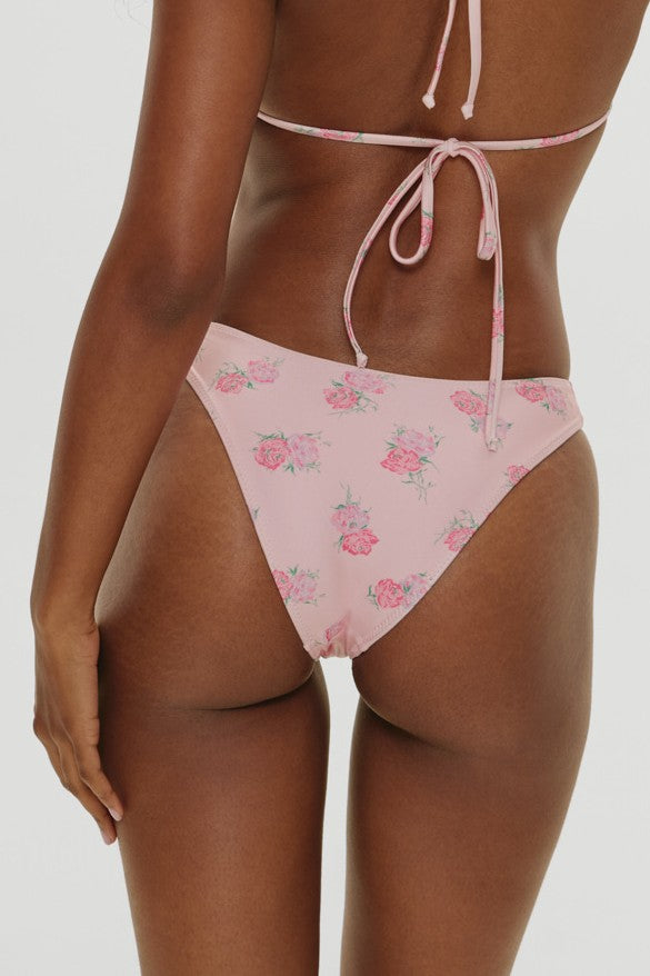 A woman is shown from the back wearing the Frankies Bikinis Fresh Rose Dove Satin Bottom, a light pink bikini bottom with a rose floral pattern and tied straps, offering classic coverage that enhances her beach style against a plain white background.