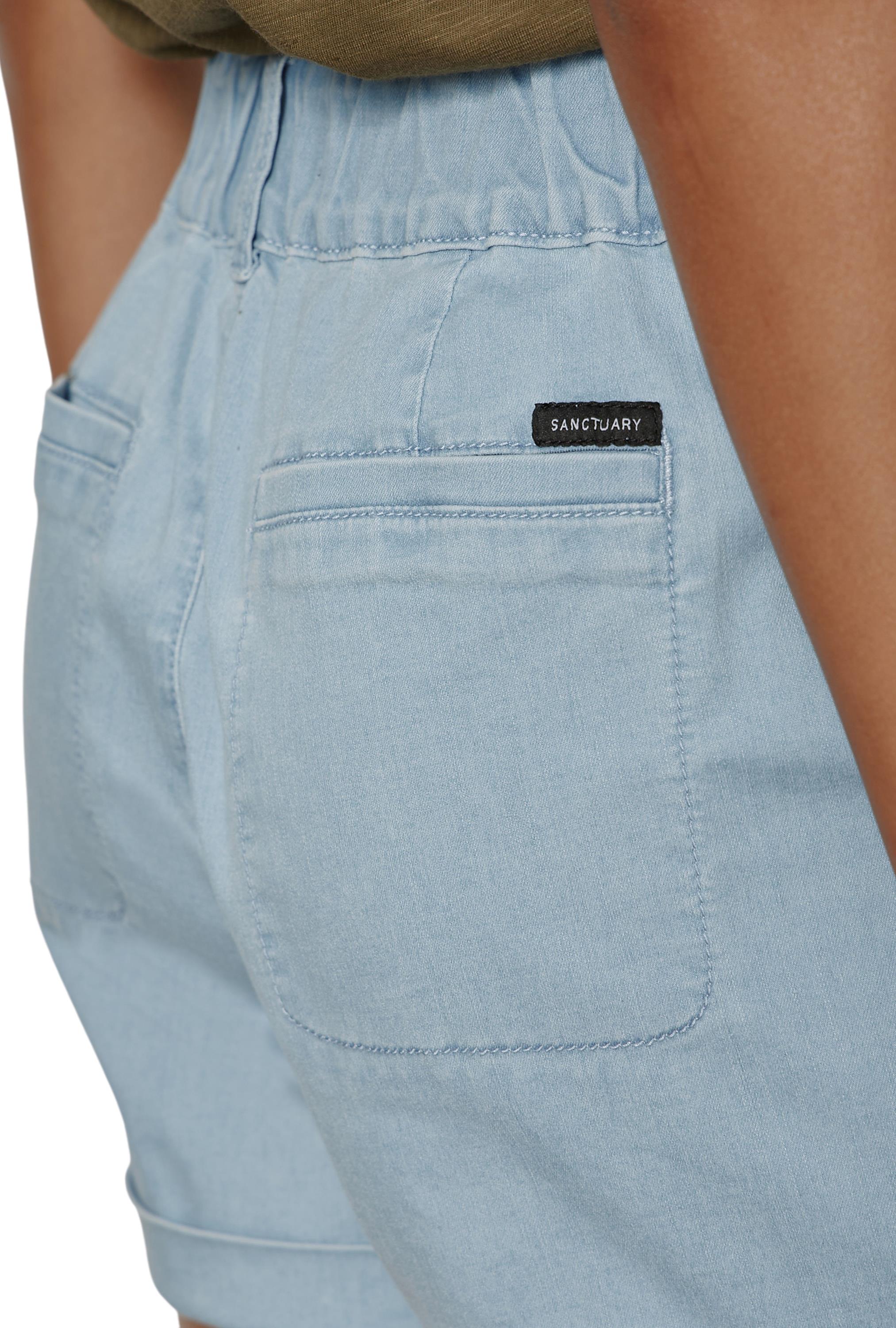 Close-up of a person wearing Sanctuary's Wander On Short in light blue denim, featuring an elastic waistband, back patch pockets, and a black Sanctuary label above the right pocket for added style and comfort.