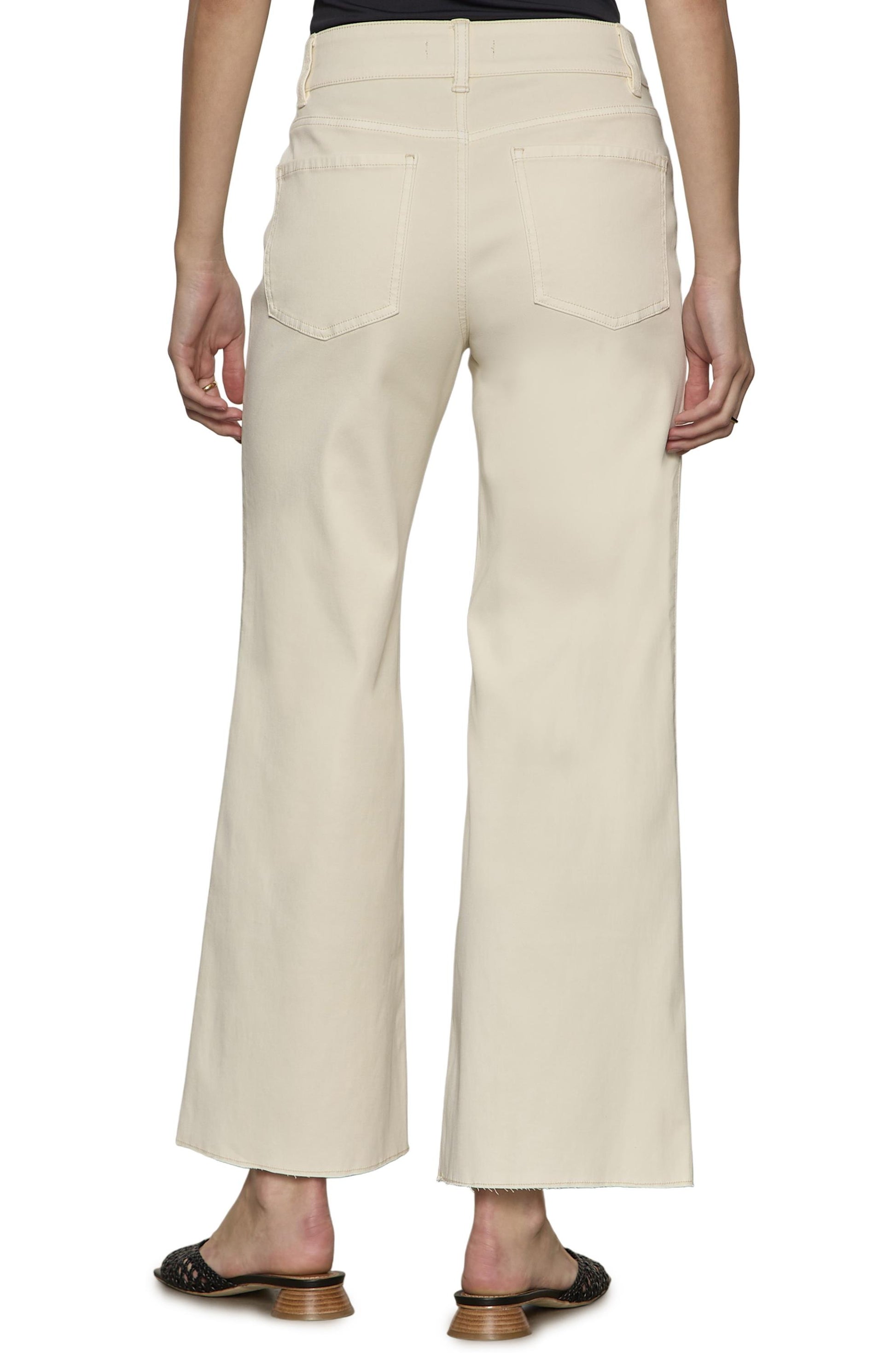 A person is seen from behind wearing Sanctuary's Skipper Crop: high-waisted, cream wide-leg jeans with two back pockets, raw edge hem, and black heeled sandals.