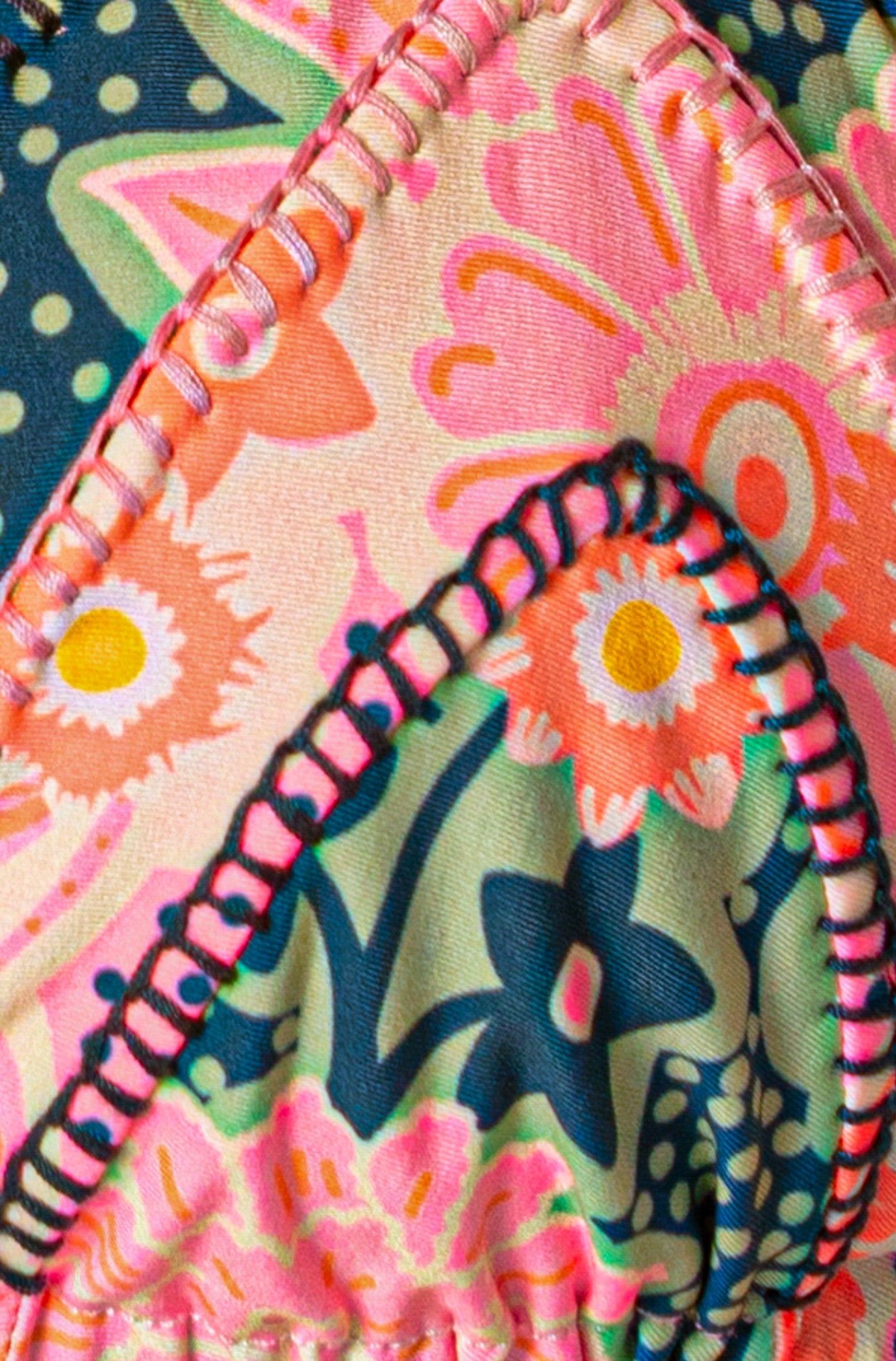 Close-up of the Maaji Blush Floral Alana Top, showing its vibrant pink, orange, blue, and green floral pattern with visible stitching and overlapping fabric sections.