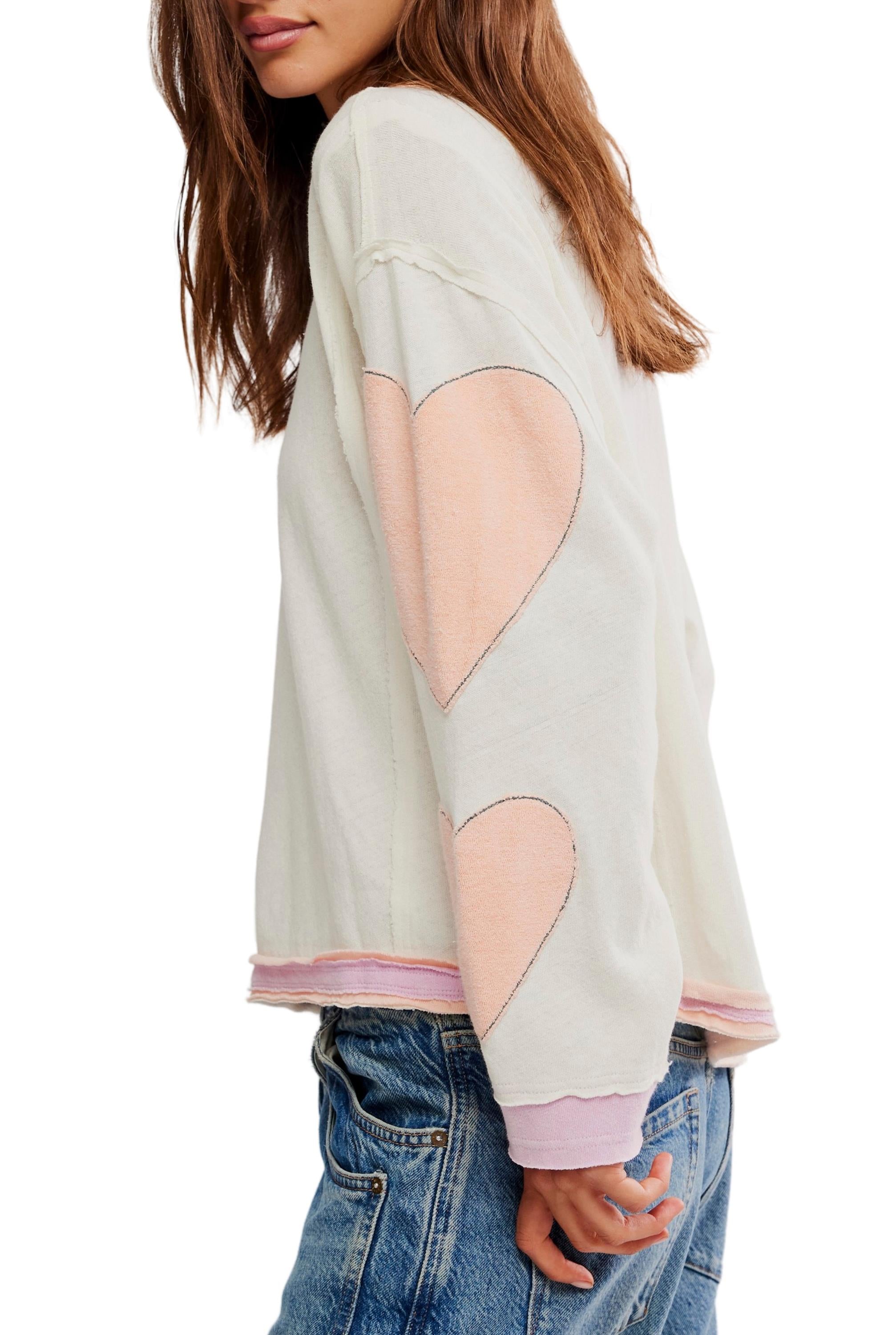 A woman with long brown hair wears the Free People Youre A Star Tee and blue jeans. She stands sideways, one hand in her pocket, highlighting the unique detailing on her sleeve.