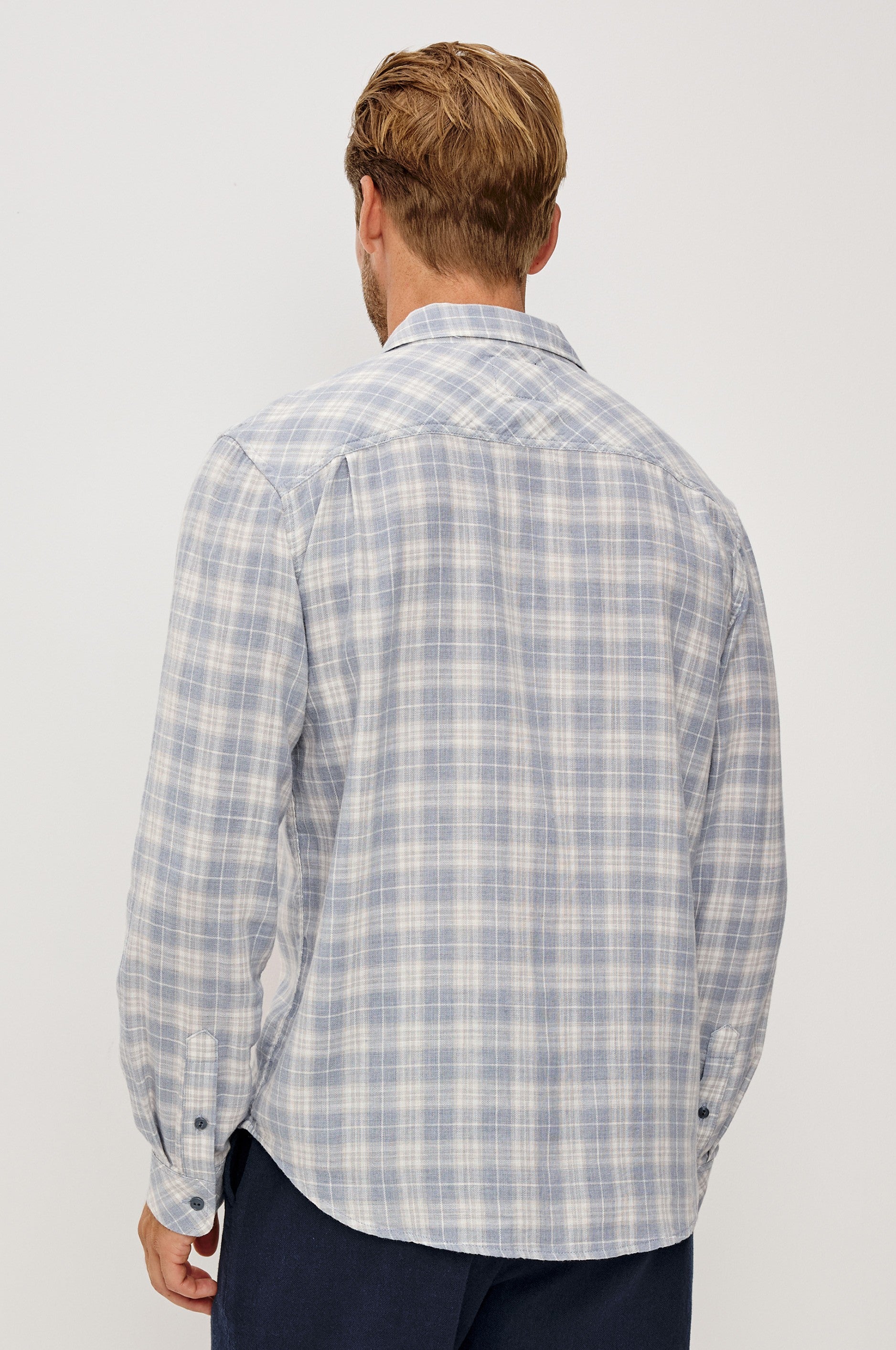 A man with light brown hair is shown from behind, wearing the Rails Wyatt Thatch Cloud Cream Plaid Woven shirt in a relaxed fit, paired with dark pants, standing against a plain light background.