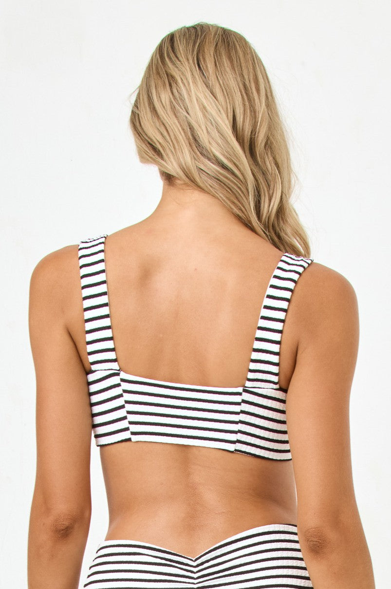 A woman with long blonde hair is shown from the back, wearing the L*Space Sail Along Stripe Marlee Top—a matching black and white striped bikini—against a plain white background.