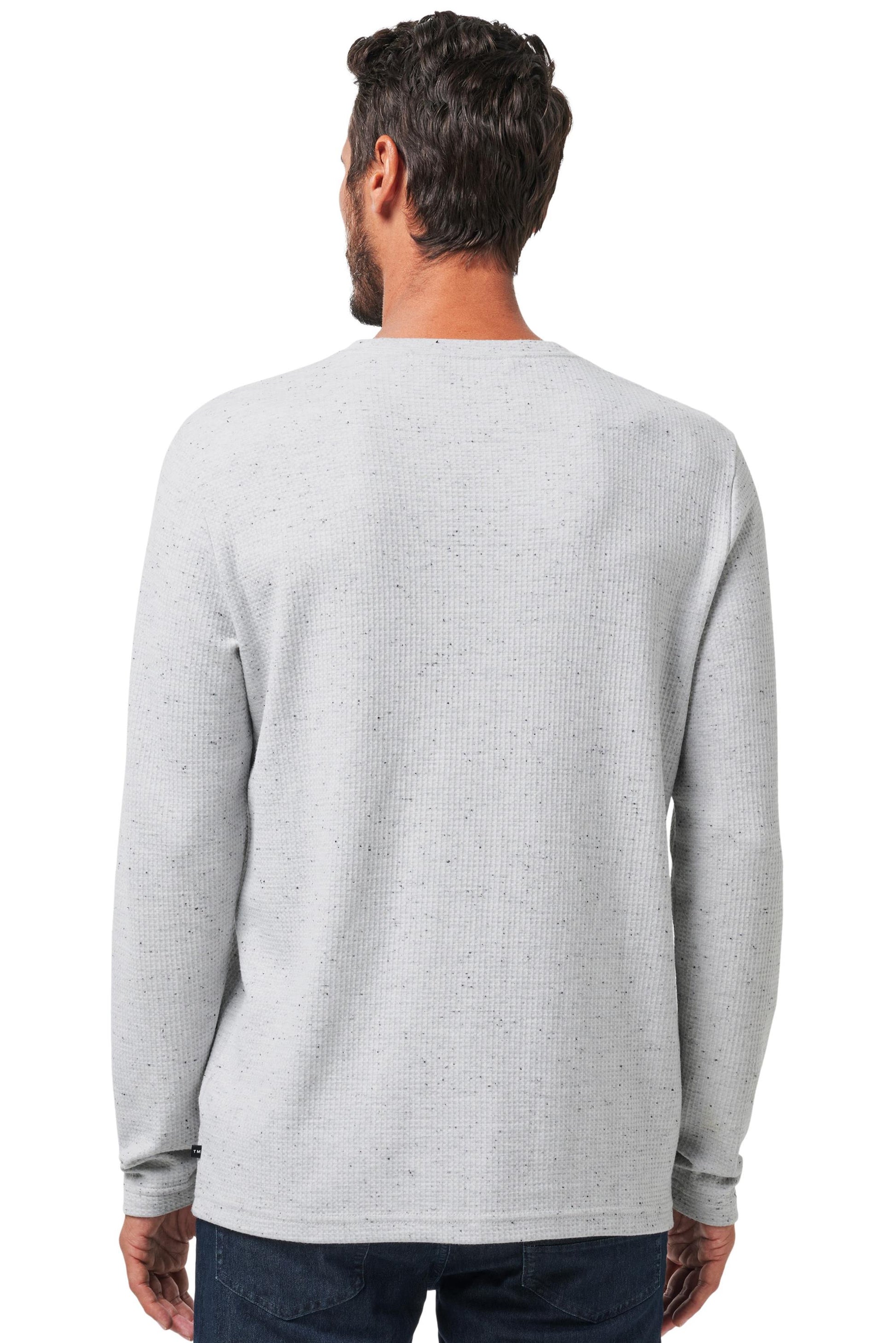 A man with short dark hair is seen from behind wearing the TravisMathew Cloud Waffle Crew, a light gray long-sleeve shirt, paired with dark blue jeans against a plain white background.