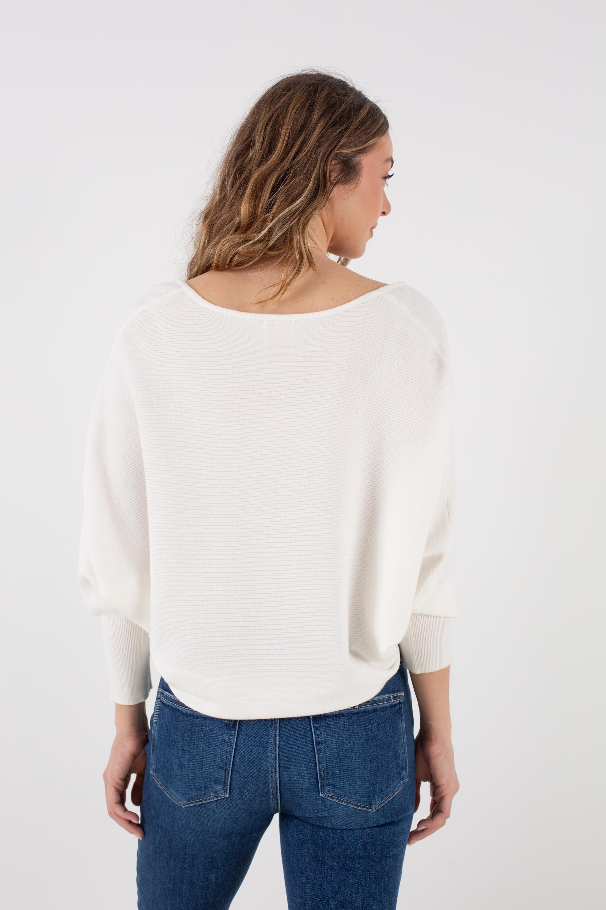 A woman with long, wavy hair is seen from behind against a plain white background, wearing the Kerisma Dolman Ryu V Neck in Ivory paired with blue jeans.