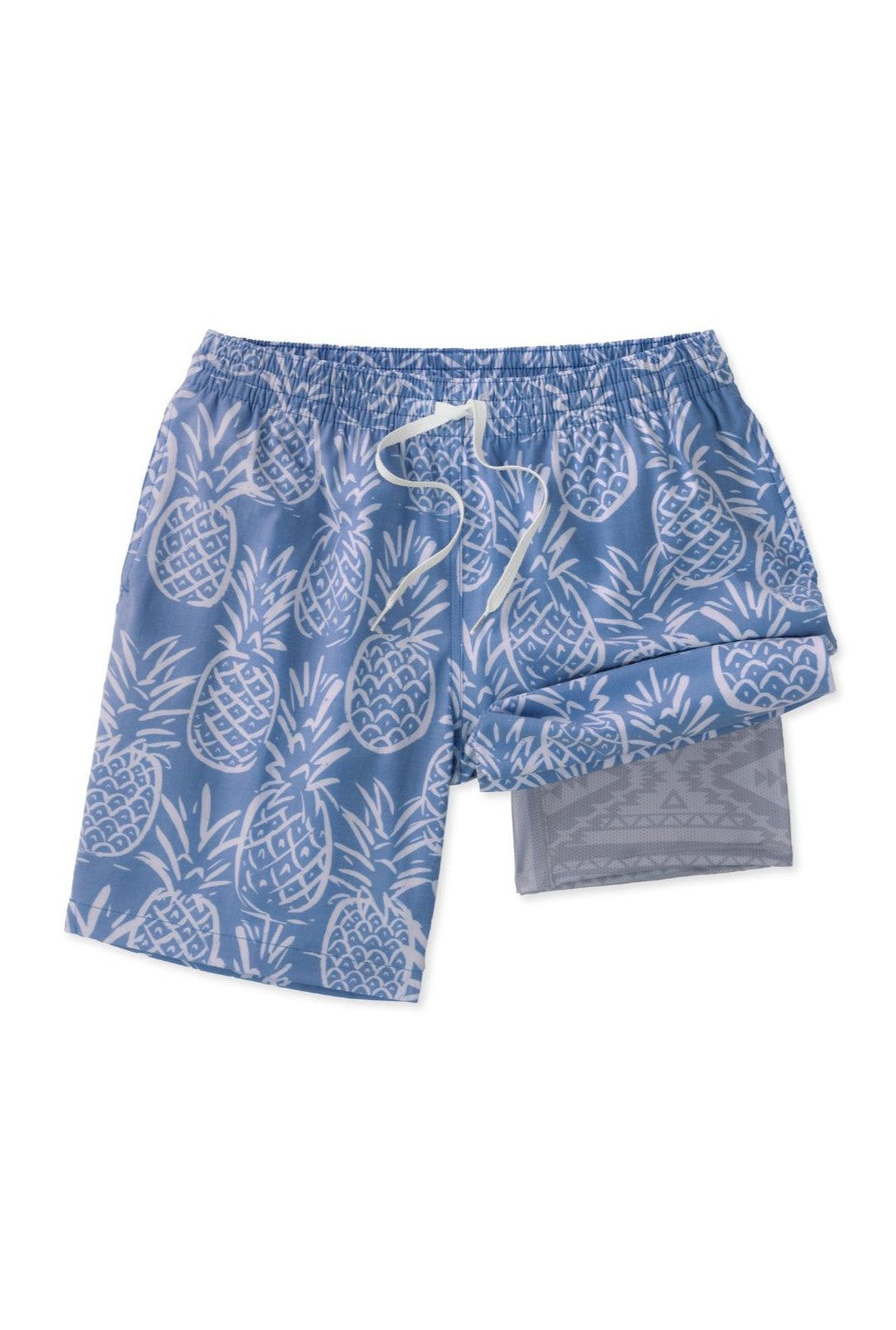 The Thighnapples 5.5 Inch Lined Swim by Chubbies features blue swim trunks with a white pineapple print, elastic waistband, white drawstring, quick-dry fabric, and gray mesh lining visible with one leg folded up.
