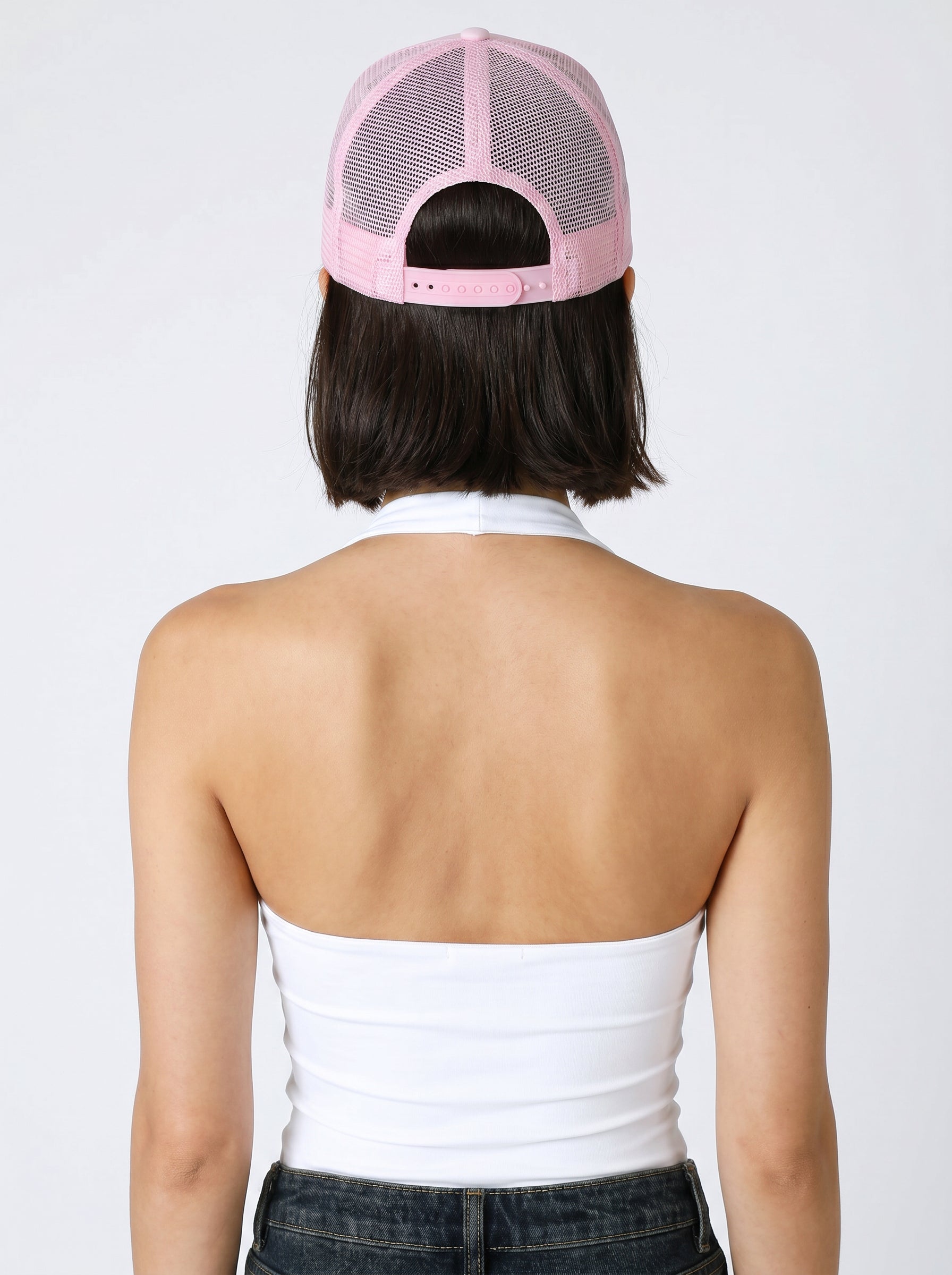 A person with shoulder-length dark hair wears the South Moon Under Cowgirls & Cocktails Trucker Hat backwards and a white halter top, facing away on a plain white background—an effortlessly casual look that’s perfect for a country concert.